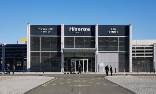 Moderne Fassade des Hisense Europe Innovations- und Forschungszentrums mit Glasfront, Sonnenschutzlamellen und einigen Personen, die vor dem Haupteingang im Freien stehen