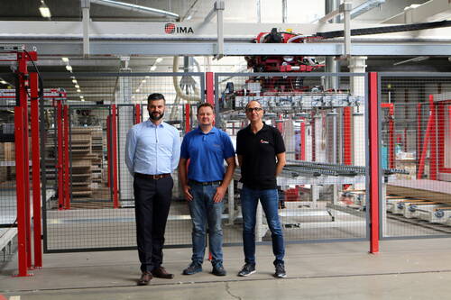 Drei Mitarbeiter posieren vor einer großflächigen, automatisierten Produktionsanlage in einer modernen Fabrikhalle
