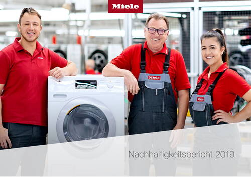 Drei Miele-Mitarbeitende in roter Arbeitskleidung präsentieren lächelnd eine moderne Waschmaschine in einer hellen Fabrikumgebung zum Nachhaltigkeitsbericht 2019