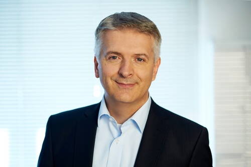 Mittelalterlicher Mann im Businessanzug lächelt freundlich in heller Büro-Umgebung in die Kamera