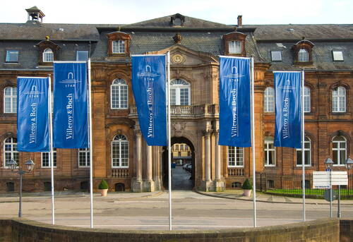 Historisches Verwaltungsgebäude mit barocker Fassade, davor mehrere blaue Villeroy-&-Boch-Fahnen im Wind
