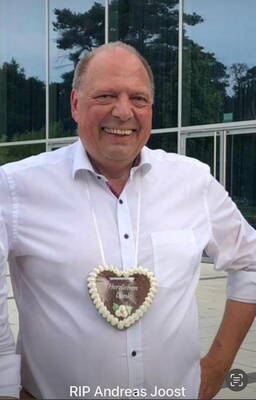 Lächelnder Mann im weißen Hemd trägt draußen vor einer Glasfassade ein herzförmiges Lebkuchenherz mit der Aufschrift „Herzlichen Dank“ um den Hals