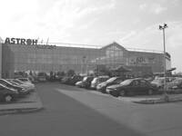 Großer Glaseinkaufsmarkt mit voll belegtem Parkplatz und vielen abgestellten Autos an einem leicht bewölkten Tag