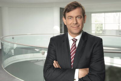 Geschäftsmann im Anzug mit verschränkten Armen steht selbstbewusst in einem modernen, hellen Bürogebäude mit Glasbrüstung im Hintergrund