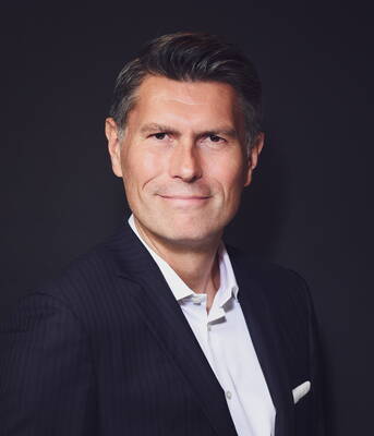 Mittelalterlicher Mann im dunklen Nadelstreifenanzug mit weißem Hemd lächelt selbstbewusst vor schwarzem Hintergrund in einem professionellen Porträt.