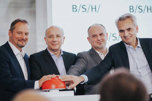 Vier Manager im Anzug lächeln in die Kamera, während sie gemeinsam symbolisch einen großen roten Startknopf vor dem BSH-Logo drücken.