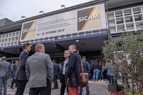 Besuchergruppe steht vor dem Eingang der Möbelzuliefermesse SICAM 2019 in Pordenone und unterhält sich unter dem großen Veranstaltungsbanner.