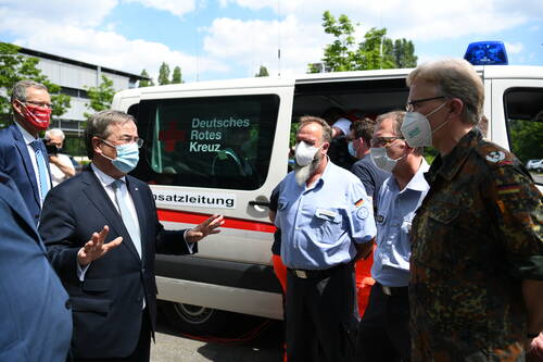 Politiker spricht mit Einsatzkräften des Deutschen Roten Kreuzes und der Bundeswehr vor einem Einsatzleitfahrzeug, alle mit Schutzmasken im Freien.