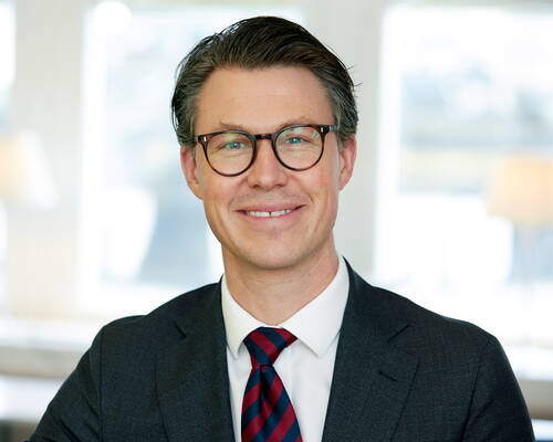 Lächelnder Geschäftsmann mit Brille und Anzug in einem hellen, modernen Büro