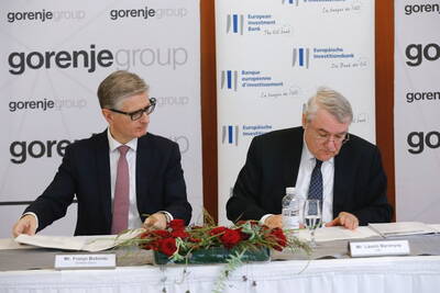 Zwei Geschäftsleute unterzeichnen Vertragsdokumente an einem Konferenztisch mit Blumenarrangement vor Bannern der Gorenje Group und der Europäischen Investitionsbank.