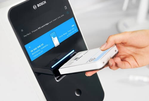 Hand schiebt eine Testkartusche in ein modernes Bosch-Diagnosegerät mit digitalem Display für Laborauswertungen