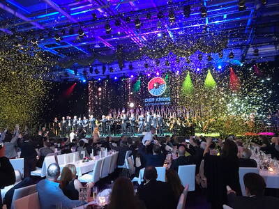 Festlich beleuchtete Galaveranstaltung mit großem Chor und Orchester auf der Bühne, Konfettiregen und applaudierendem Publikum an elegant gedeckten Tischen