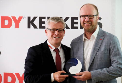 Zwei lächelnde Männer im Anzug halten gemeinsam einen Reddy-Küchen-Award vor einer Werbewand mit Firmenlogo.