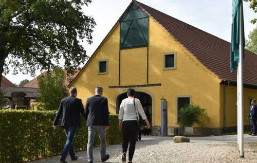 Drei Personen gehen auf ein gelbes, umgebautes Scheunengebäude mit rotem Satteldach und großem Eingang im Innenhof zu