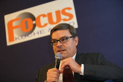 Mittelalterlicher Mann im Anzug spricht mit Mikrofon vor dunkelblauem Hintergrund und einem „Focus Küche & Bad“-Logo im oberen Bildbereich