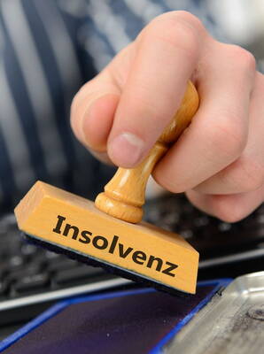 Hand drückt einen Holzstempel mit der Aufschrift „Insolvenz“ in ein Stempelkissen vor einer Computertastatur