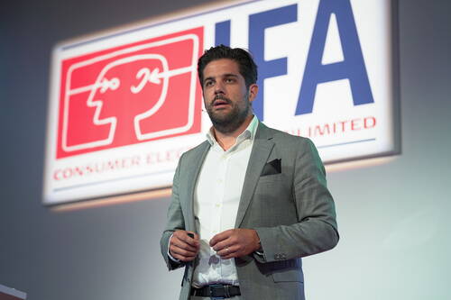 Geschäftsmann im grauen Anzug hält eine Präsentation auf der IFA-Bühne vor großem Messe-Logo im Hintergrund
