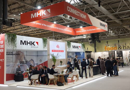 Geschäftiges Messestand‑Treffen am modernen MHK‑Group‑Stand mit Sitzgruppen, Beratungsgesprächen und großen Werbebannern unter einer hohen Hallendecke.