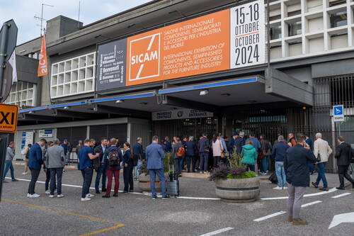 Besuchergruppe wartet vor dem zentraleingang der Möbelmesse SICAM 2024 in Pordenone unter großen Bannern mit Terminhinweisen und Willkommensgrüßen in mehreren Sprachen