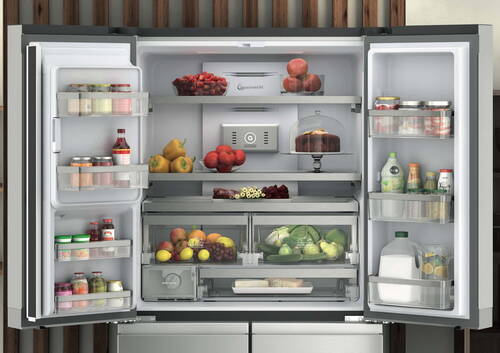 Offener, moderner Kühlschrank mit ordentlich sortierten frischen Lebensmitteln, Getränken, Obst, Gemüse und einer Torte auf einer Glasplatte