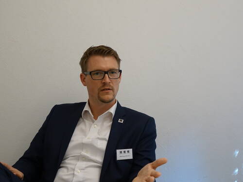 Mann im Anzug sitzt vor einer weißen Wand und gestikuliert nachdenklich während eines Gesprächs