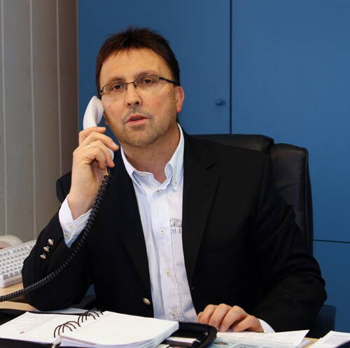 Geschäftsmann im Anzug telefoniert im Büro und macht sich Notizen in einem aufgeschlagenen Terminplaner auf dem Schreibtisch
