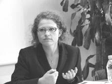 Nachdenkliche Frau mit Brille und lockigen Haaren spricht gestikulierend in einem Besprechungsraum
