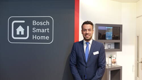 Mitarbeiter im Anzug präsentiert einen Bosch-Smart-Home-Messestand mit großem Logo und vernetzter Haussteuerung im Hintergrund