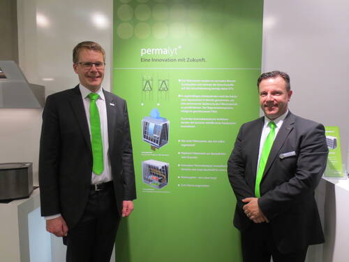 Zwei Geschäftsleute im Anzug mit leuchtend grünen Krawatten präsentieren vor einem grünen Messedisplay das Filtersystem „Permalyt – Eine Innovation mit Zukunft“