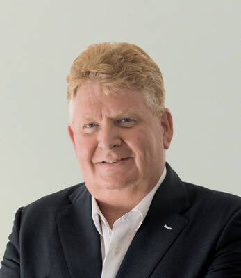 Älterer Mann mit blondem, gewelltem Haar und dunklem Anzug lächelt freundlich in die Kamera vor hellem Hintergrund