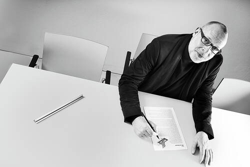 Älterer Mann mit Brille lehnt sich über einen Konferenztisch und unterschreibt ein Dokument, während ein Lineal alleine auf der sonst leeren Tischfläche liegt.