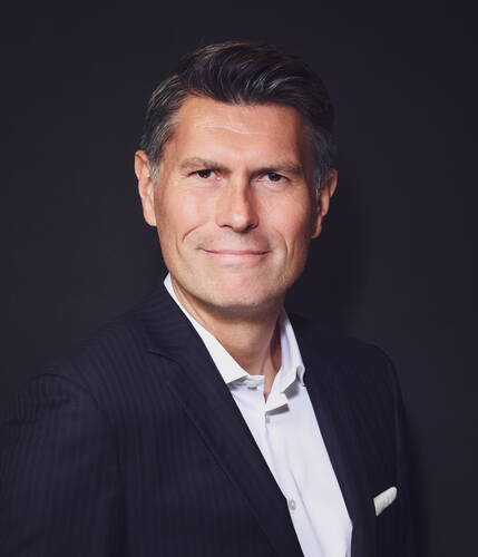 Mittelalterlicher Mann im dunklen Nadelstreifenanzug mit weißem Hemd lächelt selbstbewusst vor schwarzem Hintergrund in einem professionellen Porträt.