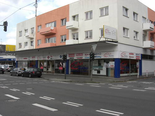 Eckgebäude mit Küchen-Outlet im Erdgeschoss und mehreren Balkonen in den oberen Etagen an einer vielbefahrenen Kreuzung