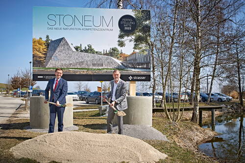 Zwei Männer im Anzug führen mit Schaufeln den Spatenstich für das neue Naturstein-Kompetenzzentrum „STONEUM“ vor einem großen Bauschild auf einem Parkplatz neben einem Teich durch.