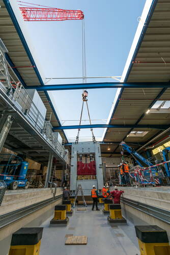 Monteure überwachen das millimetergenaue Einheben eines großen Maschinenmoduls in eine offene Industriehalle mithilfe eines roten Turmdrehkrans