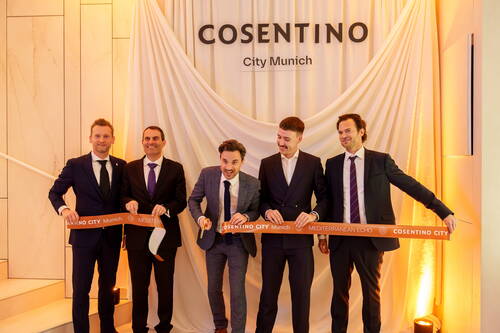 Fünf elegant gekleidete Männer durchschneiden gemeinsam ein orangenes Band bei der feierlichen Eröffnung des Showrooms „Cosentino City Munich“ vor einem drapierten Vorhang.