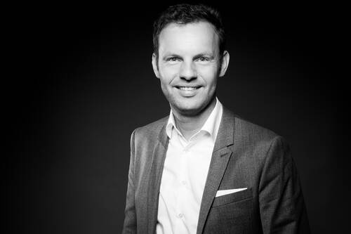 Lächelnder Mann im Anzug mit weißem Hemd in einem klassischen schwarz-weißen Portrait vor dunklem Hintergrund
