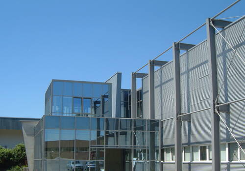 Modernes Industrie- und Bürogebäude mit großer Glasfassade und Stahlkonstruktion unter klarem blauem Himmel