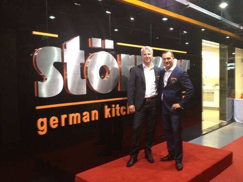 Zwei elegant gekleidete Männer stehen lächelnd auf einem roten Teppich vor einer glänzenden schwarzen Wand mit großem „stöer“ und dem Schriftzug „german kitchen“