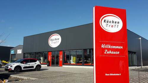 Modernes Küchenstudio „KüchenTreff“ mit großem roten Willkommensschild und geparktem Firmenauto auf dem Parkplatz.
