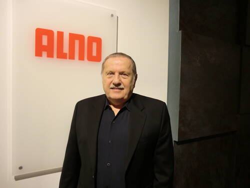 Älterer Mann im dunklen Anzug steht lächelnd vor einer hellen Wand mit rotem ALNO-Logo.