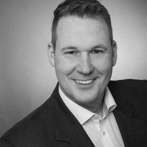 Lächelnder Mann im Anzug bei einem professionellen Schwarzweiß-Bewerbungsfoto vor neutralem Hintergrund