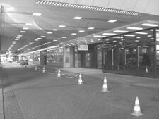 Überdachter Eingangsbereich eines modernen Gebäudes mit Glasfassade, geregelter Zufahrt und in Reihe aufgestellten Verkehrskegeln