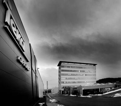 Dunkles Industrie- und Bürogebäude mit mehrstöckigem Verwaltungsbau unter bedrohlich bewölktem Himmel im Winter.