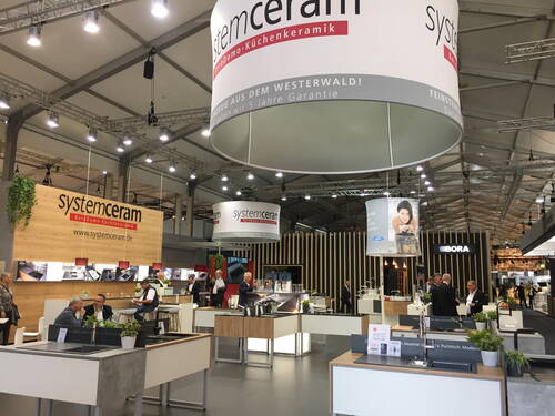 Messestand von Systemceram mit modernen Küchenarbeitsplatten und Spülen, an dem mehrere Besucher und Mitarbeiter im Gespräch stehen