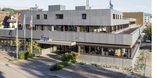 Modernes mehrstöckiges Büro- und Produktionsgebäude der Hawa Sliding Solutions mit Metallfassade, grossen Fenstern und umliegender begrünter Außenanlage an einer ruhigen Straße.