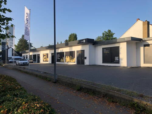 Modernes, einstöckiges Bürogebäude „cube 30“ mit großflächigen schwarzen und gelben Werbeflächen, leerem Parkplatz und geparkten Autos an einer ruhigen Straße bei klarem Abendlicht