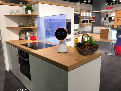 Moderner Messestand mit smarter Einbauküche, sprachgesteuertem Küchenroboter und Obstkorb auf einer Holzarbeitsplatte