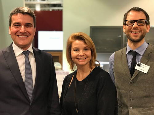 Drei lächelnde Personen in Businesskleidung stehen nebeneinander in einem hell beleuchteten Konferenzraum.
