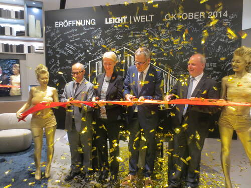 Manager und Hostessen schneiden bei der feierlichen Eröffnung der LEICHT Welt im Oktober 2014 ein rotes Band, während goldene Konfettischnipsel herabregnen.